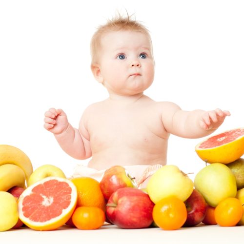 The babe in an environment of the fresh fruit, isolated on the white